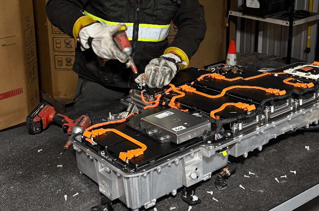 Technician in hi-vis jacket handling an EV battery pack on a workbench